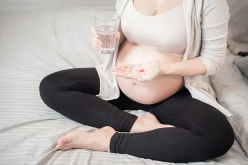 Rase naine istub voodis ja võtab oma igapäevast vitamiinide annust.